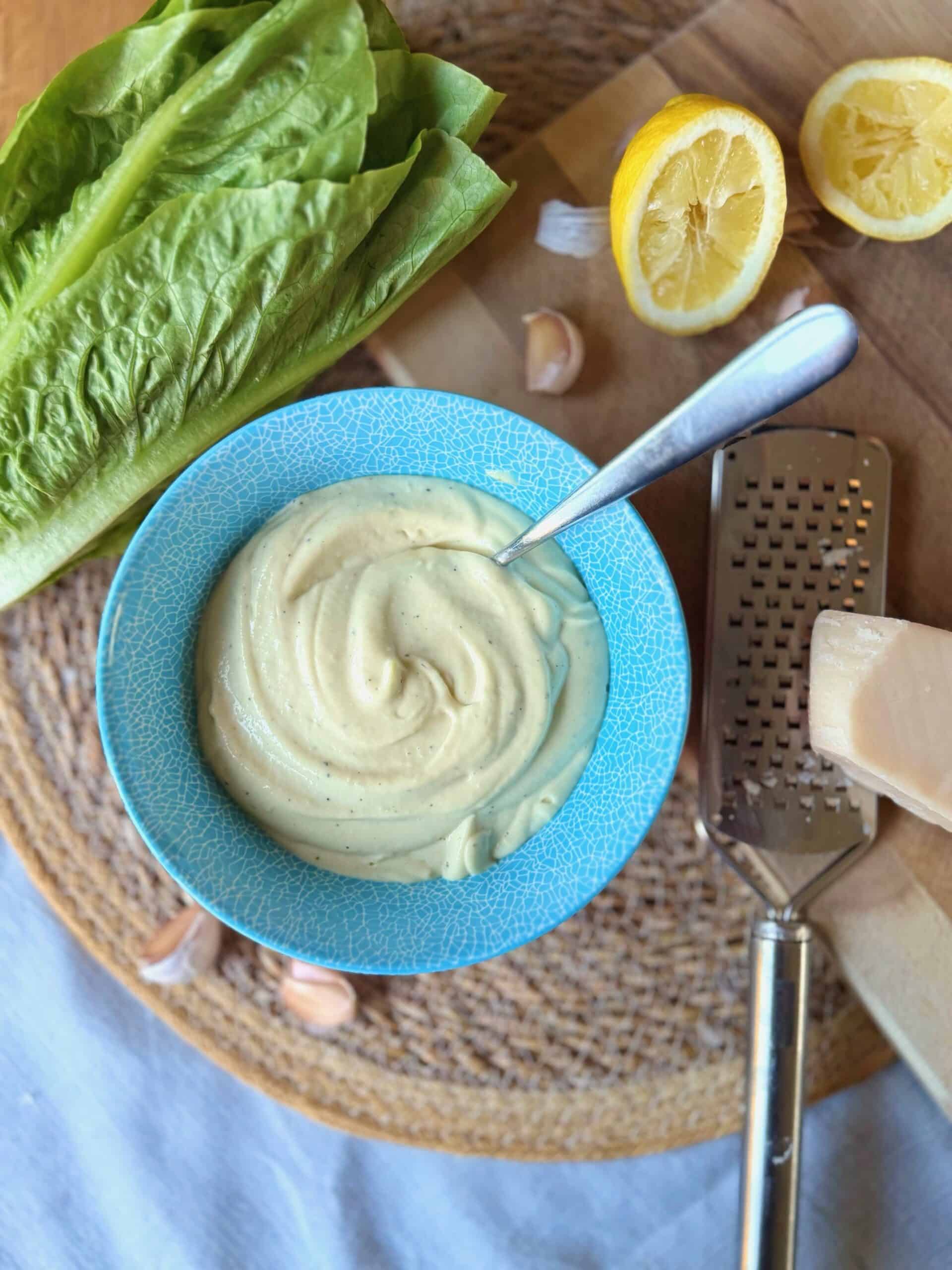 homemade caesar dressing in a bowl with green romaine lettuce, parmesan and lemon