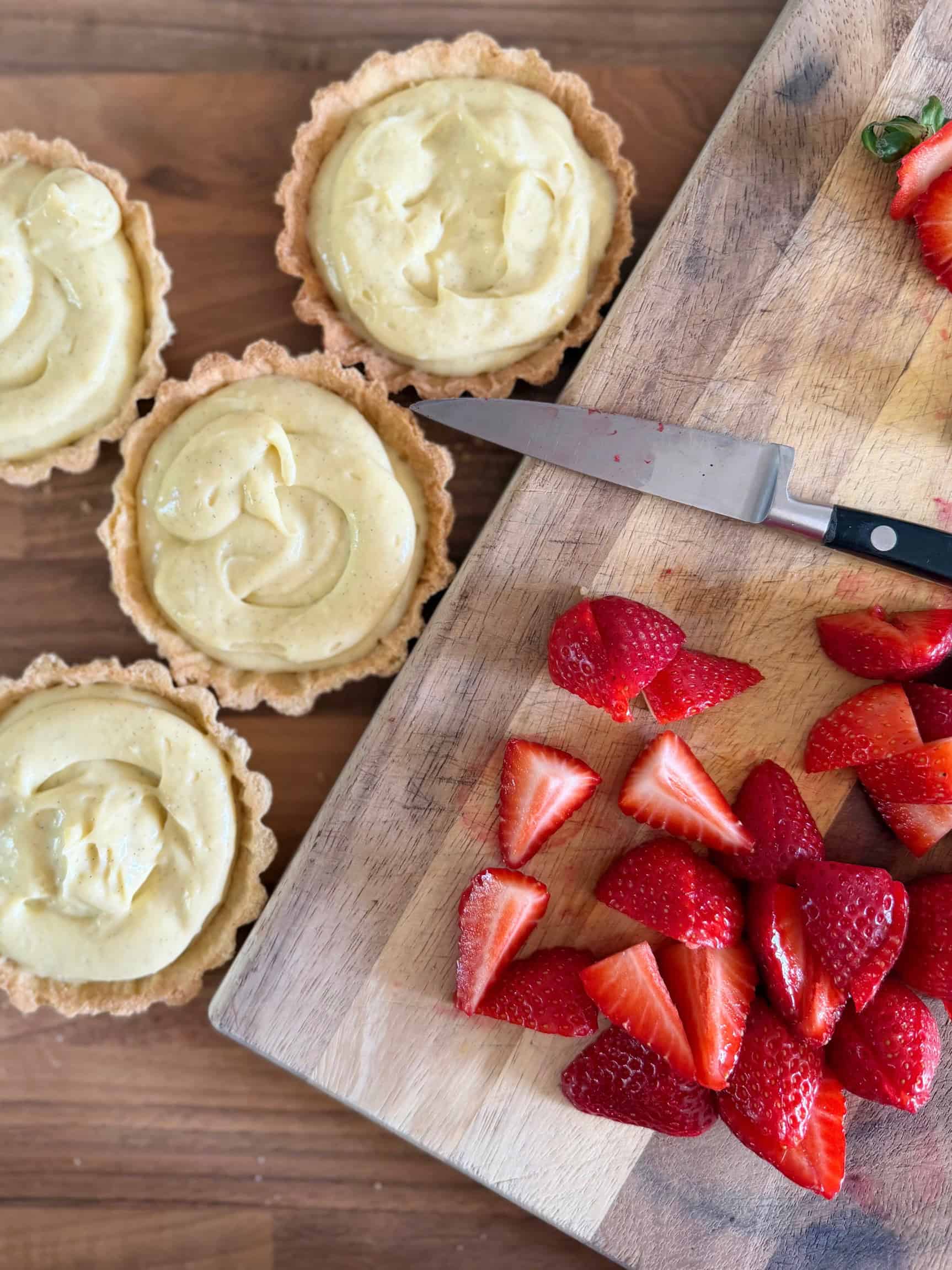 filled tart cases with pastry cream with sliced strawberries on a chopping board