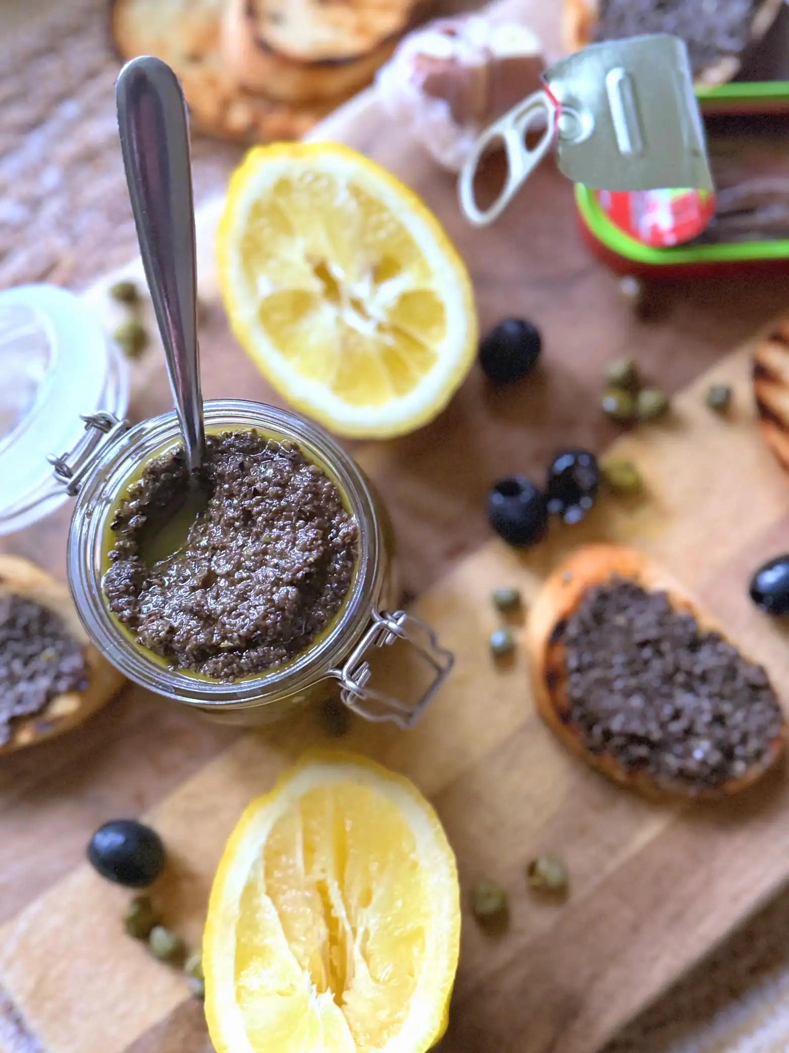 Olive tapenade on a chopping board with lemons, olives, crostinis and capers