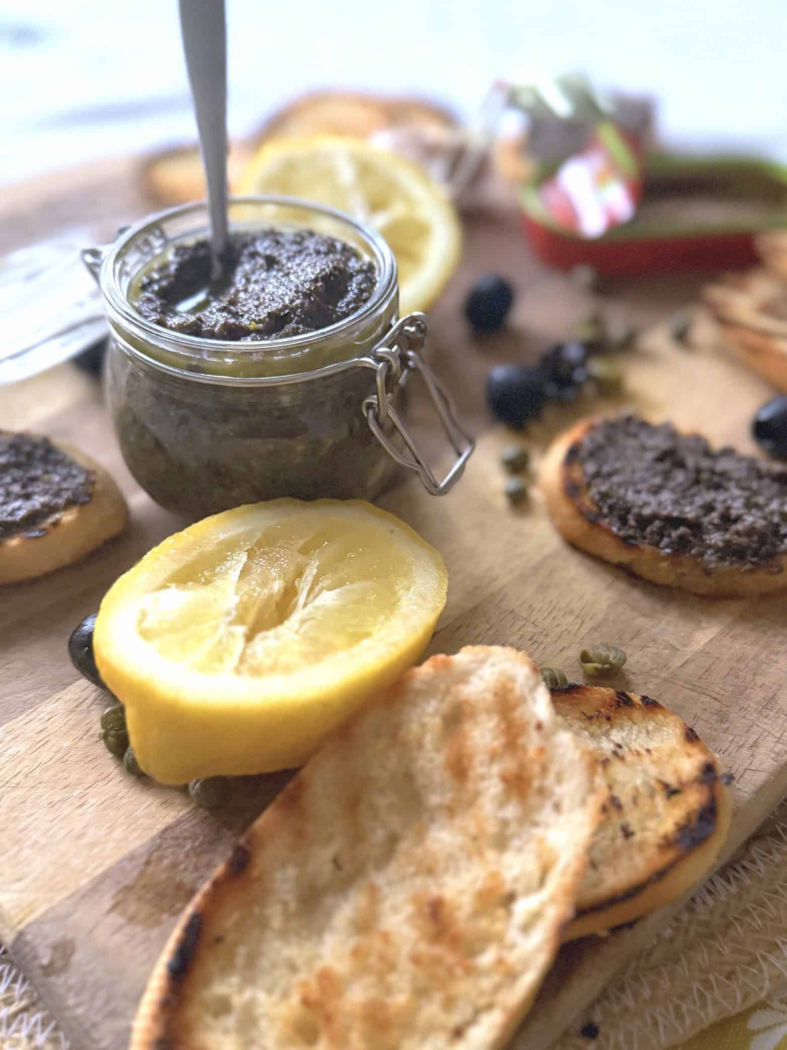 Olive tapenade in a jar with lemons and olives on a chopping board