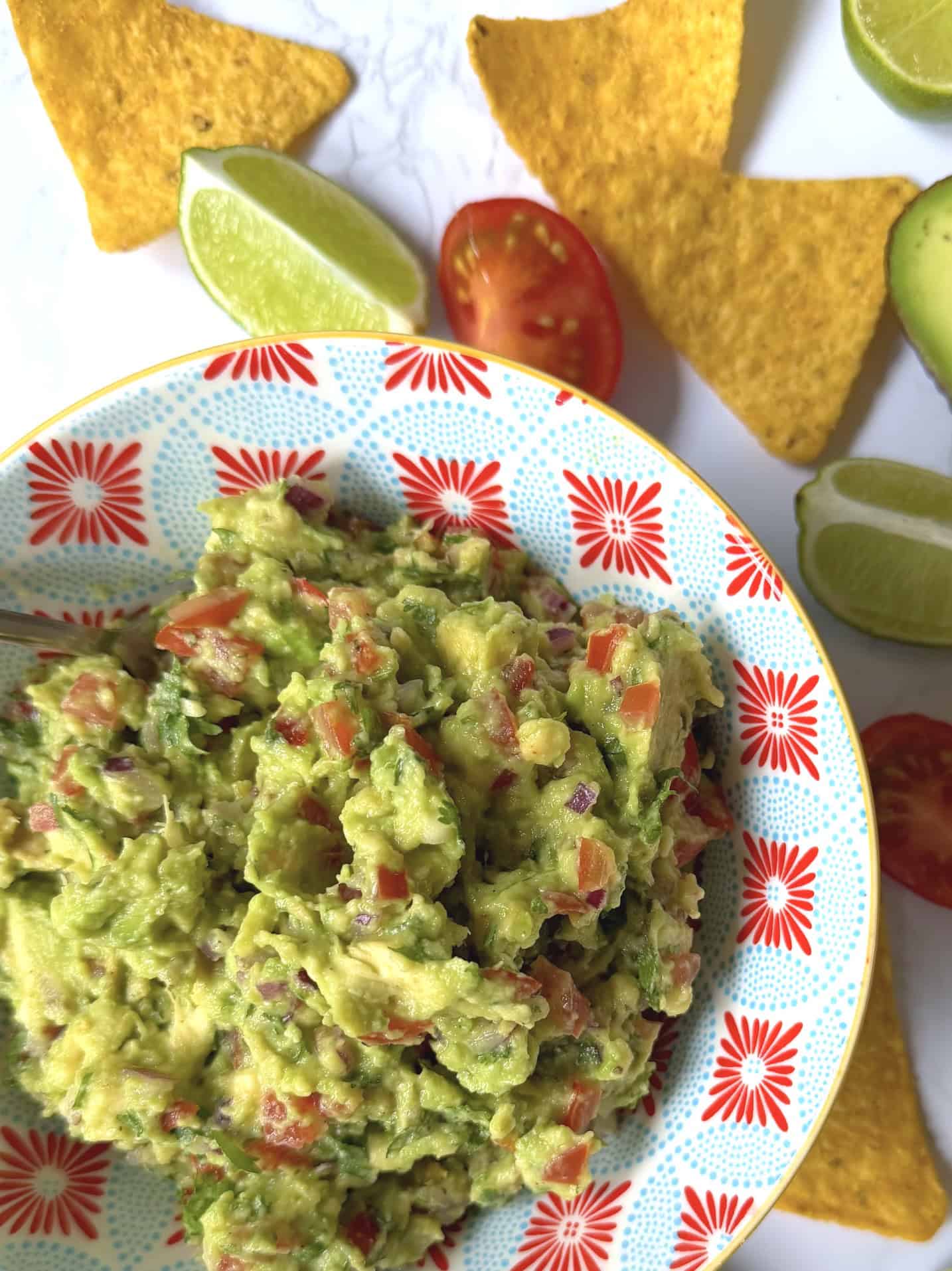 guacamole in colourful bowl with avocado and torillia chips in background