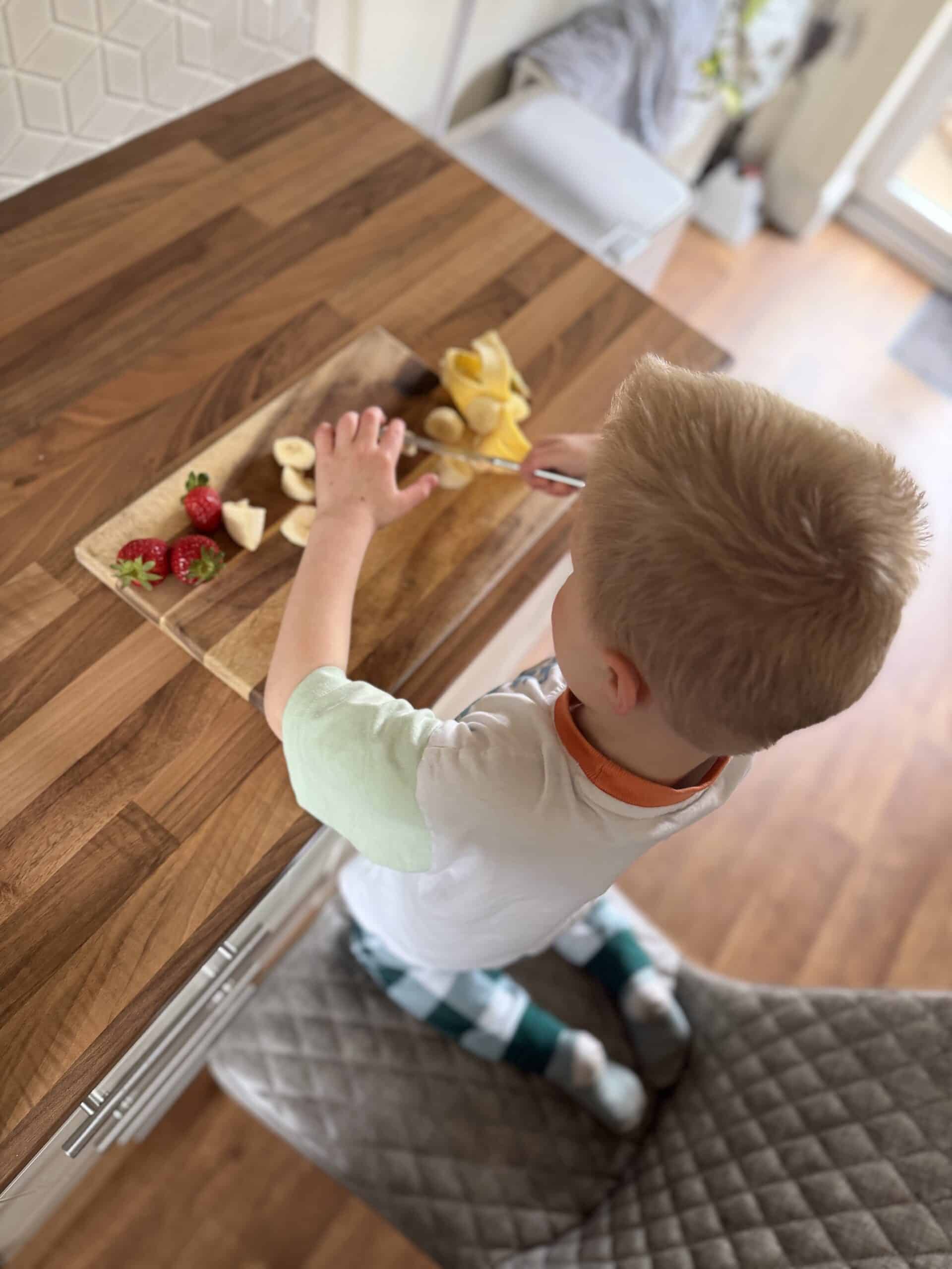 child cutting strawberries and bananas