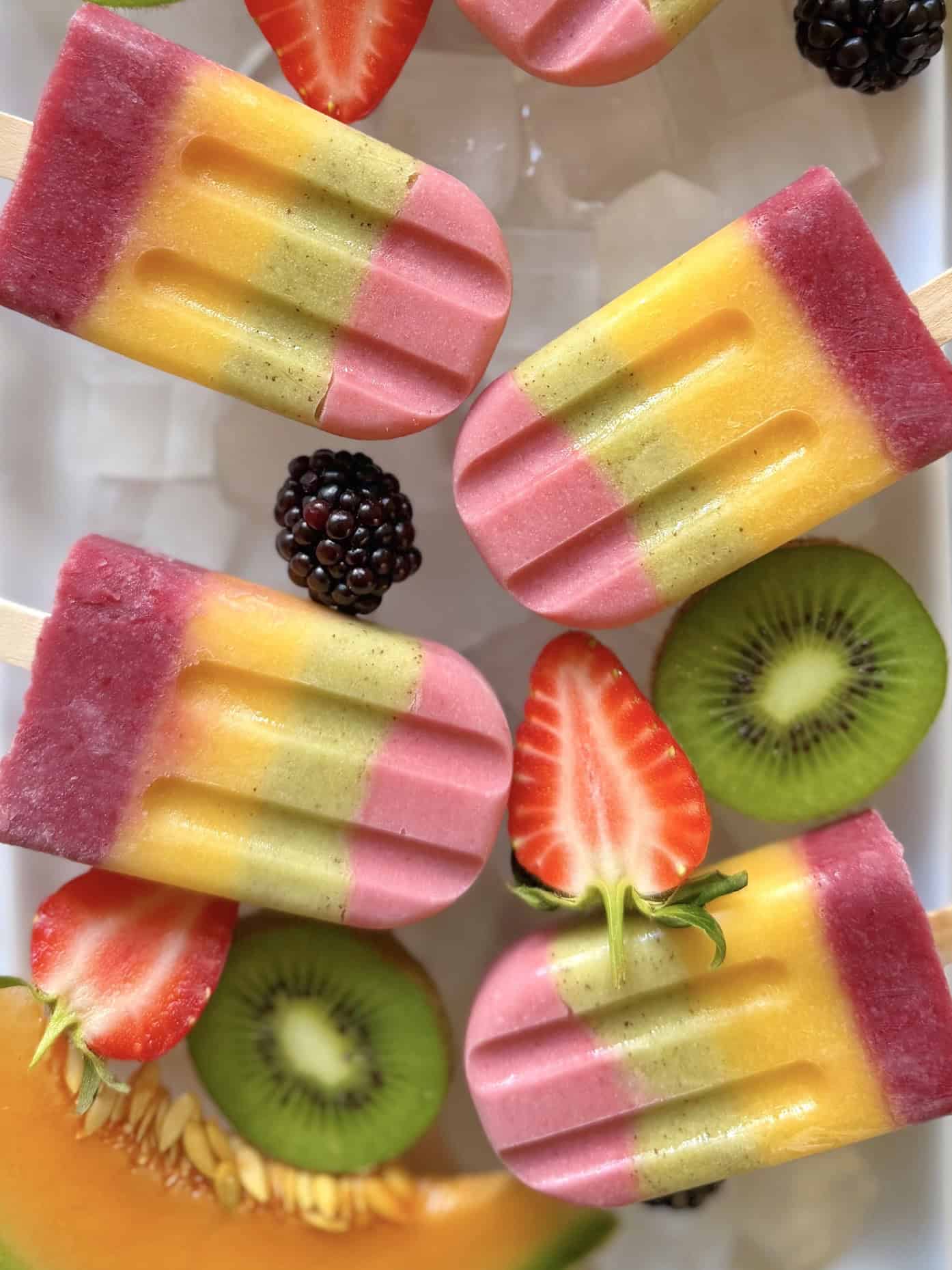 close up of rainbow popsicles on ice with fresh fruit