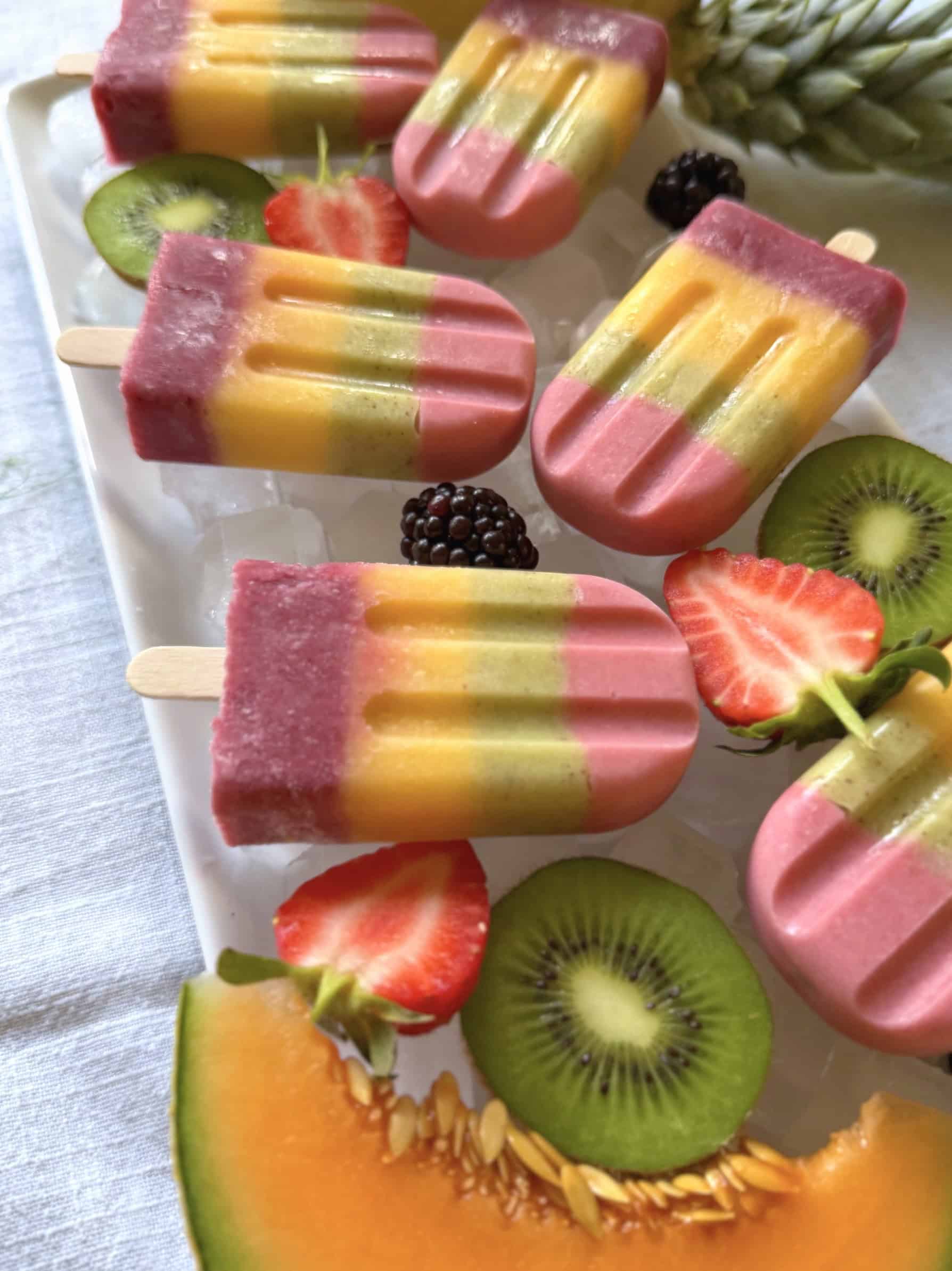Rainbow fruit popsicles on ice with fresh fruit at an angle