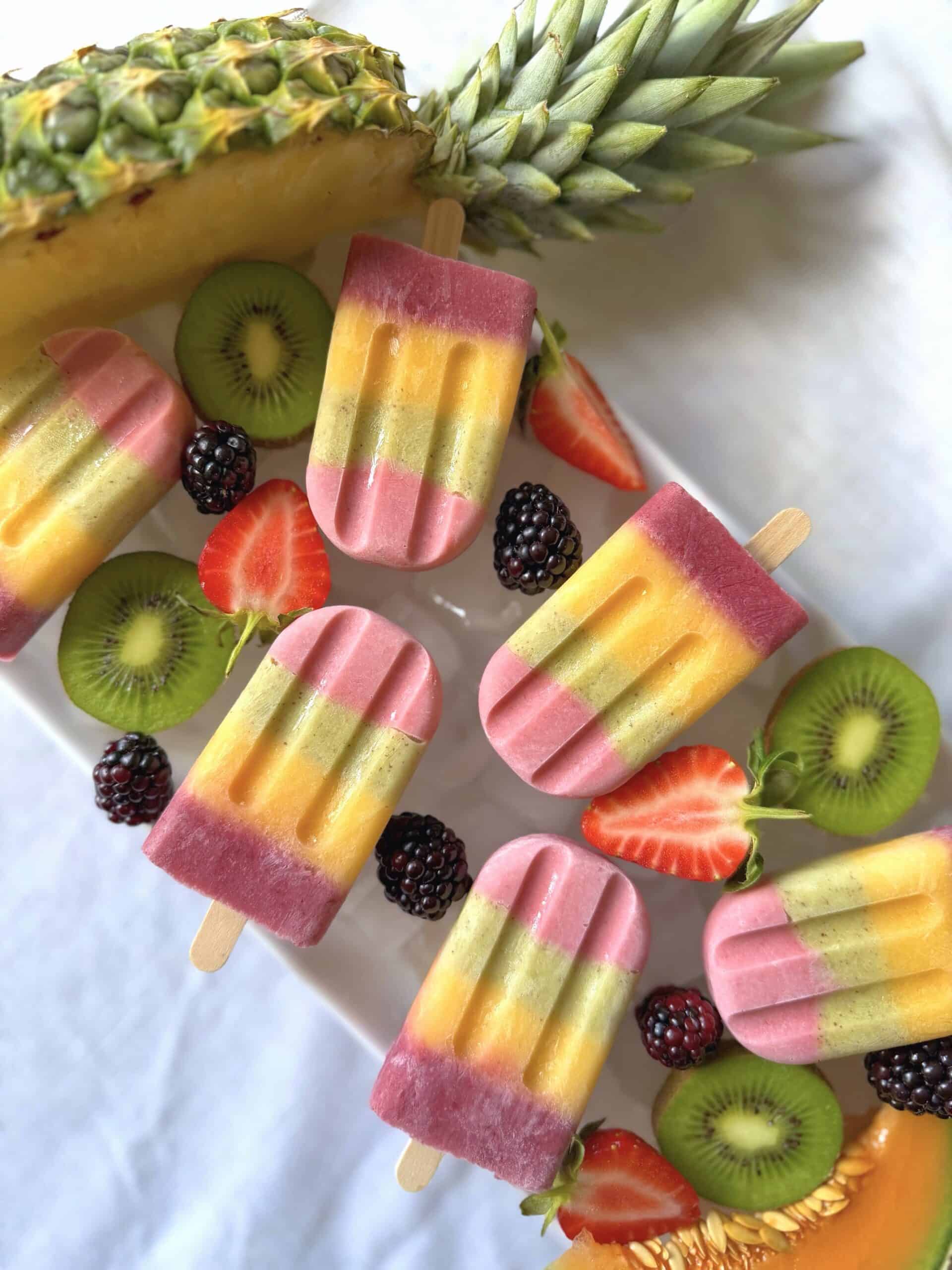 Fruit rainbow ice lollies on ice with colourful fresh fruit