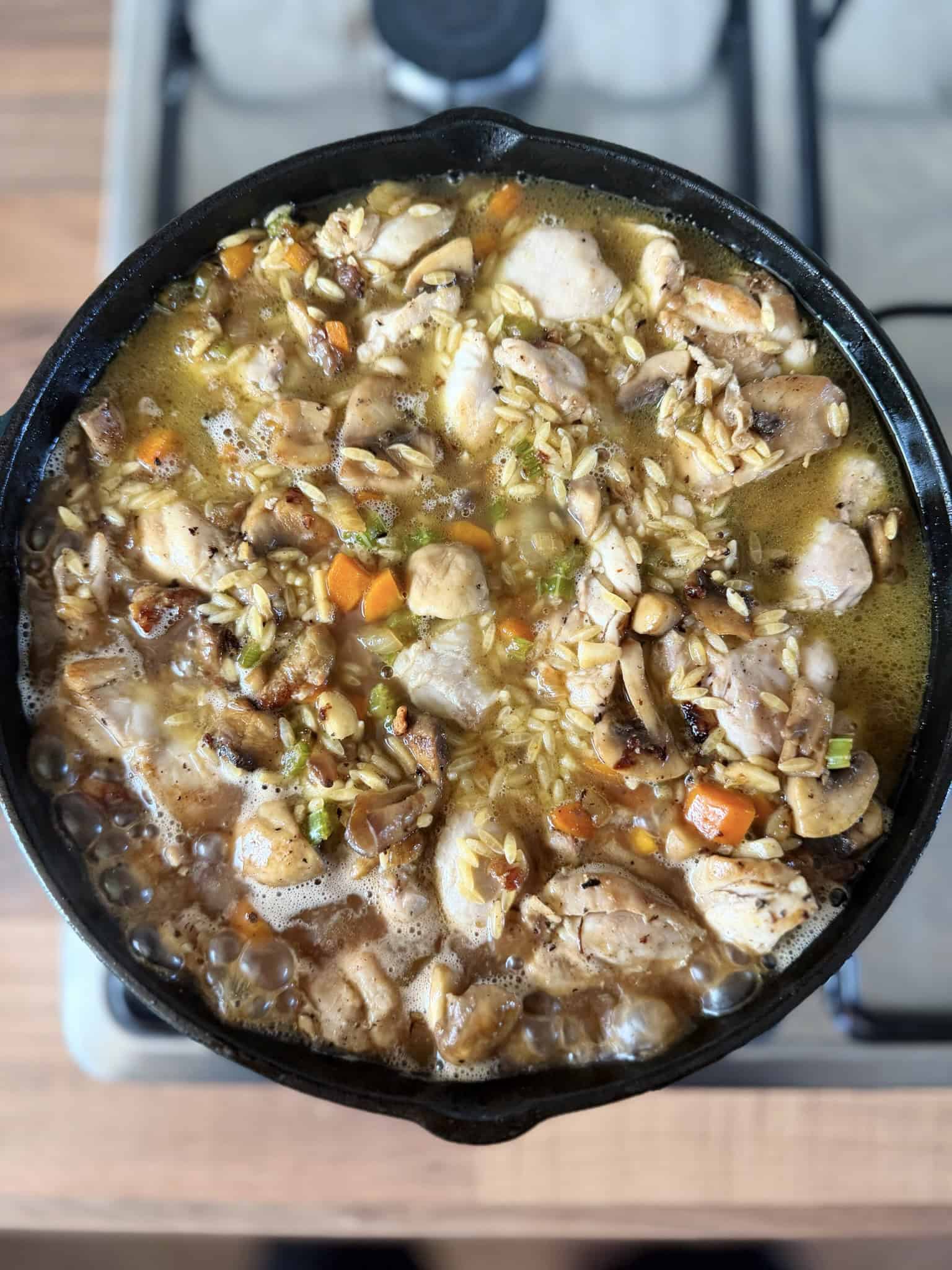 simmering stock in pan with orzo and chicken and mushrooms