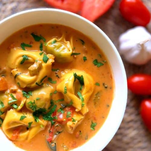 Tomato tortellini soup in a bowl with tomatoes and garlic to the side