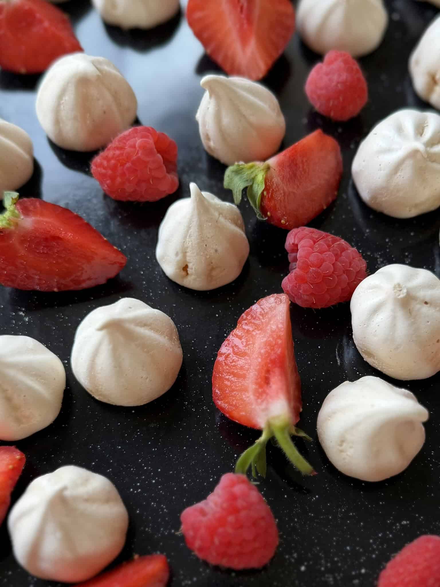 meringue kisses with red fruit on a black tray
