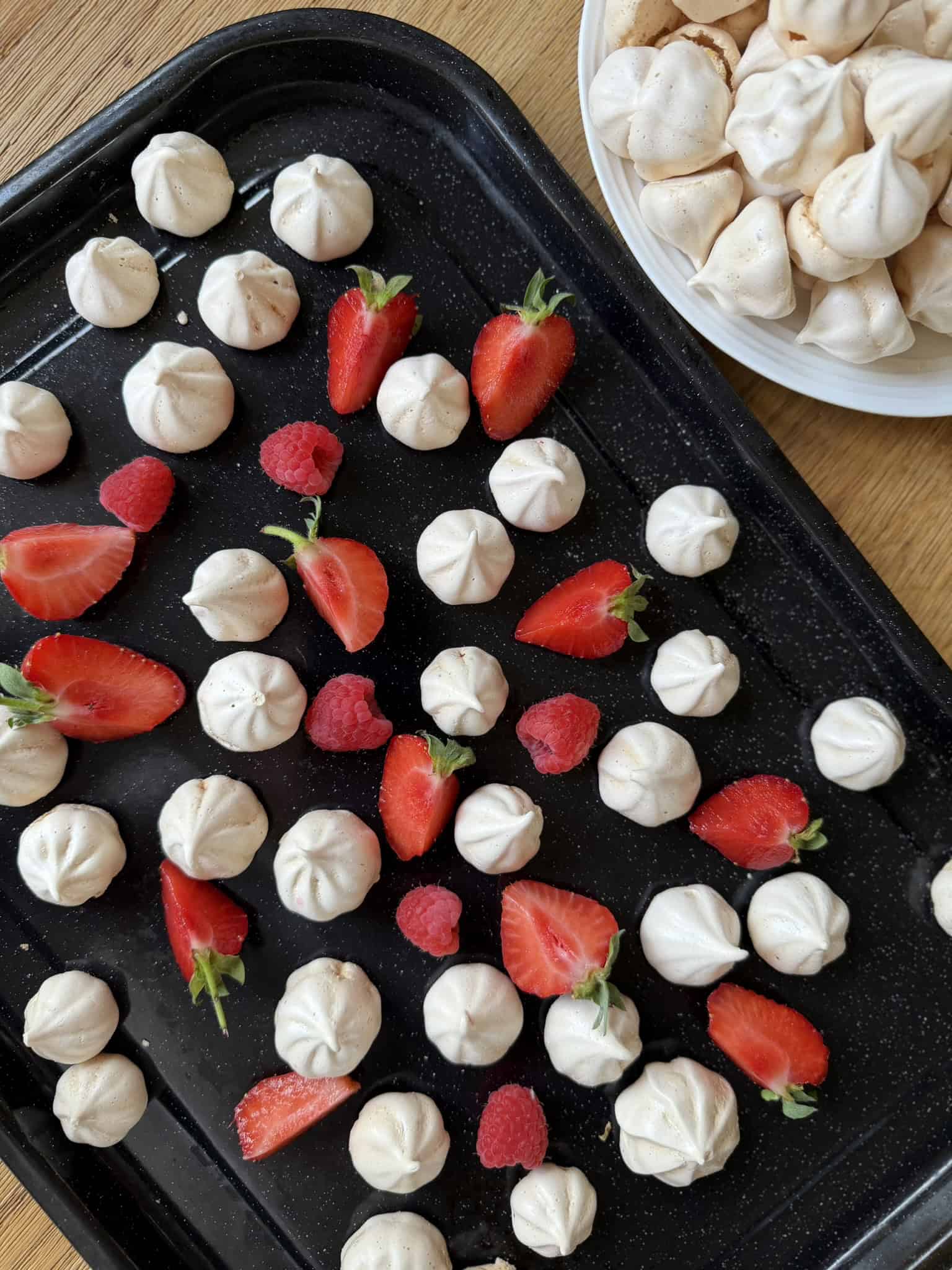 meringue kisses on a black tray with red fruit