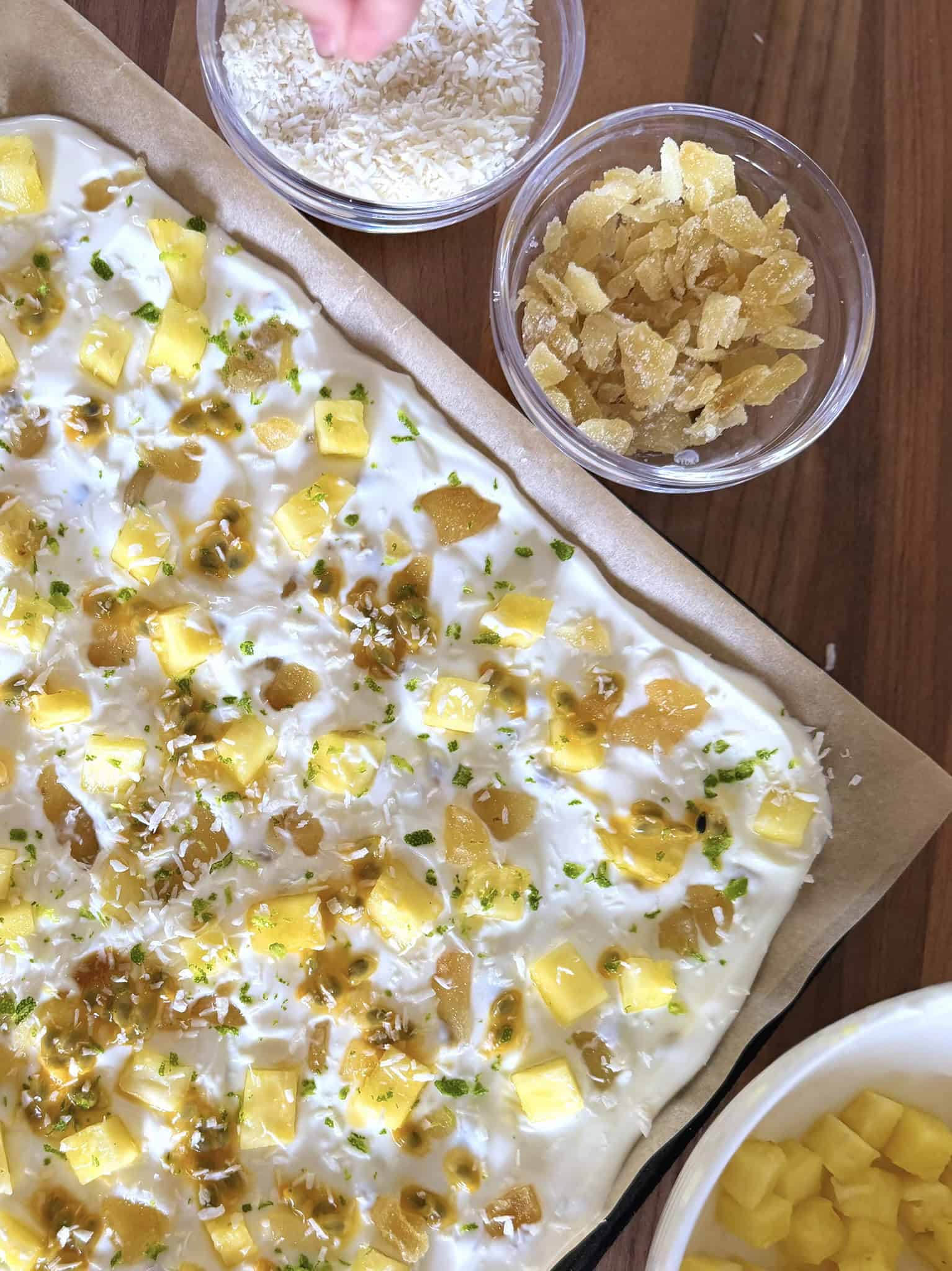 Tropical Greek yogurt bark on a tray with small bowls of pineapple and ginger