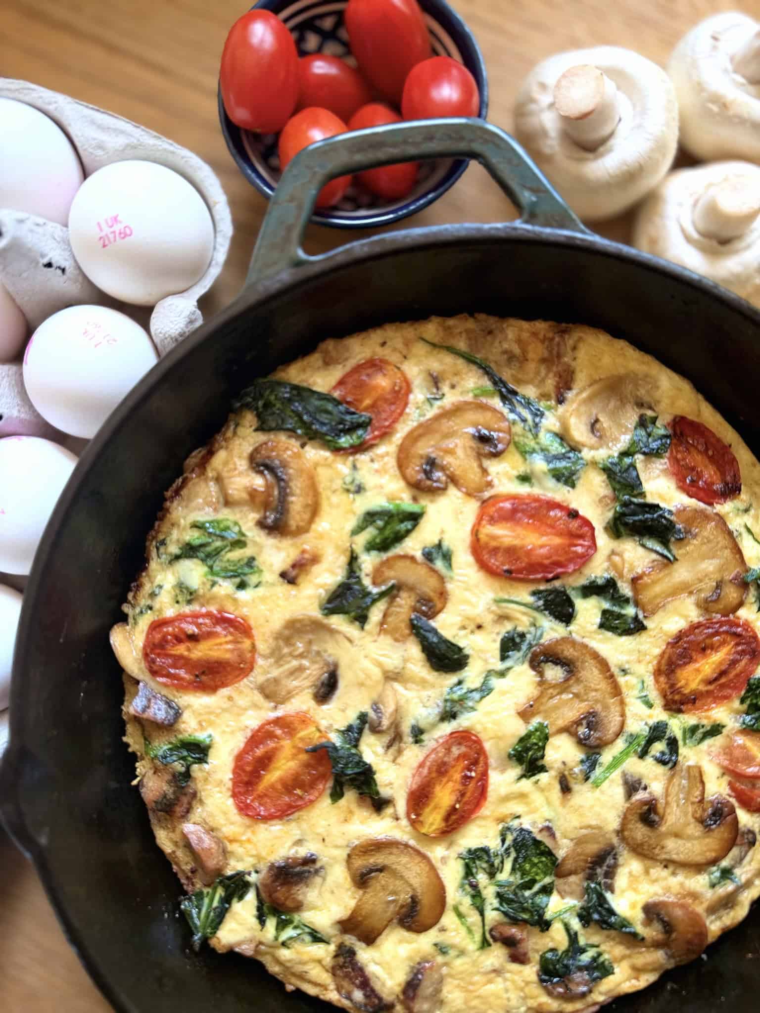 breakfast fritatta in a pan with eggs tomatoes and mushroom on the side