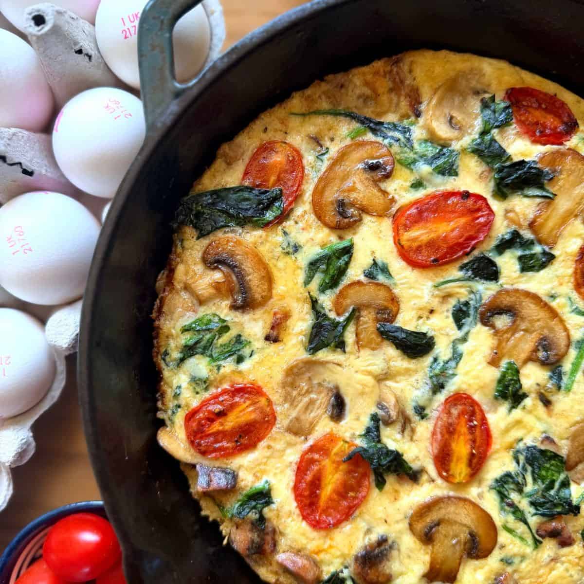 Breakfast sausage frittata in a pan with eggs and tomatoes on the side