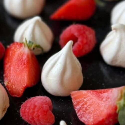 white meringue kisses on a black tray with red fruit