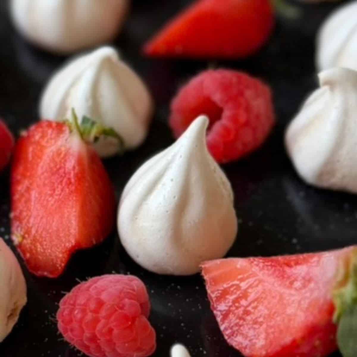 white meringue kisses on a black tray with red fruit