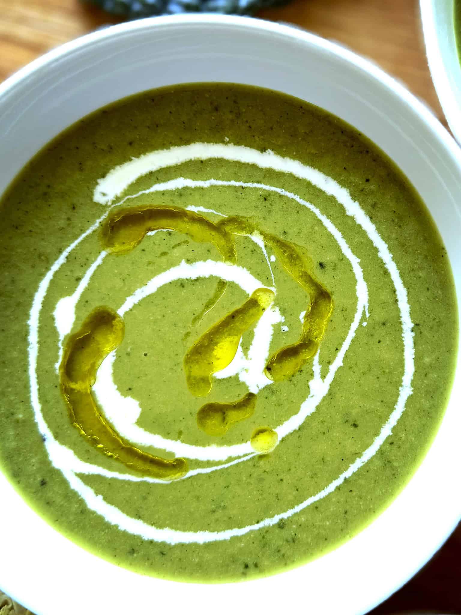 close up of green soup with drizzle of cream and oil