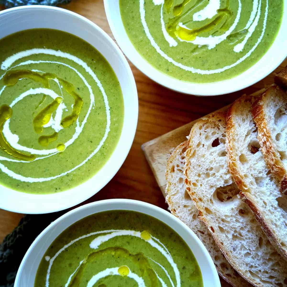 3 bowls of green soup with sour dough bread on the side